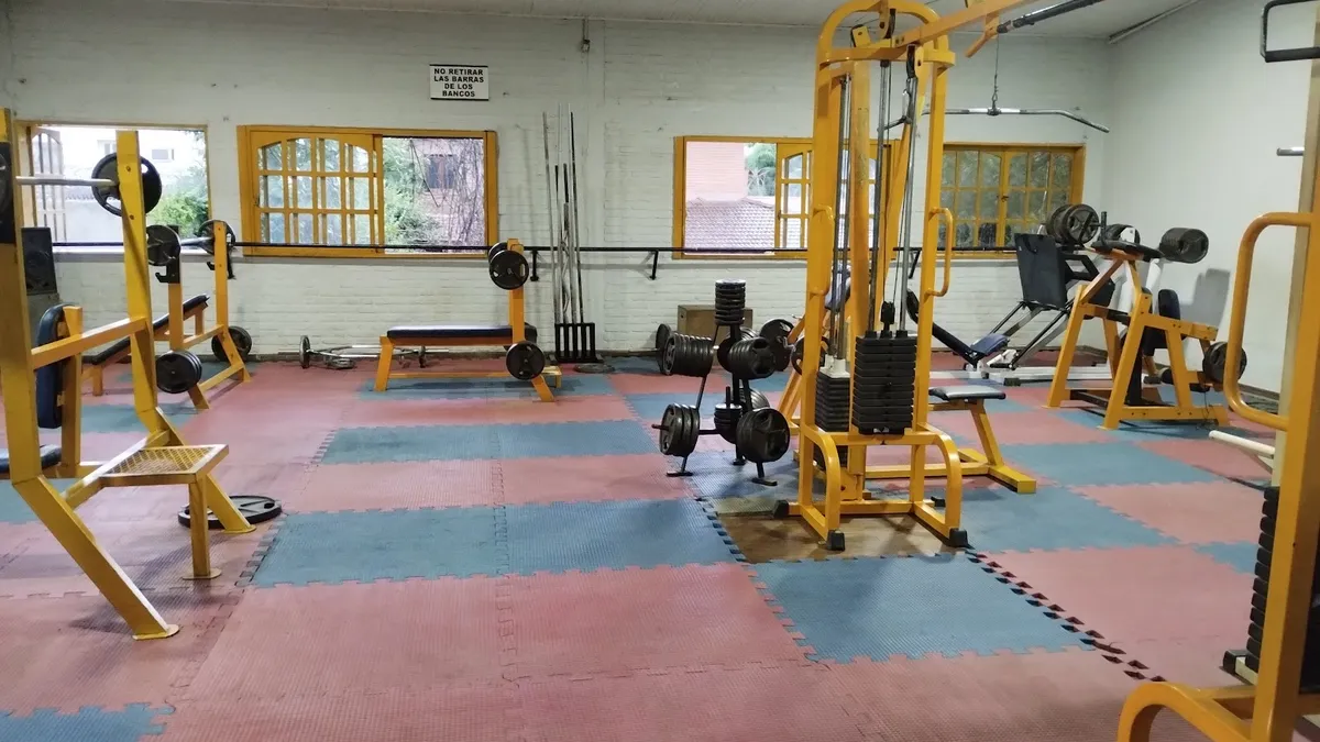 Sala de musculación con máquinas amarillas y piso de goma